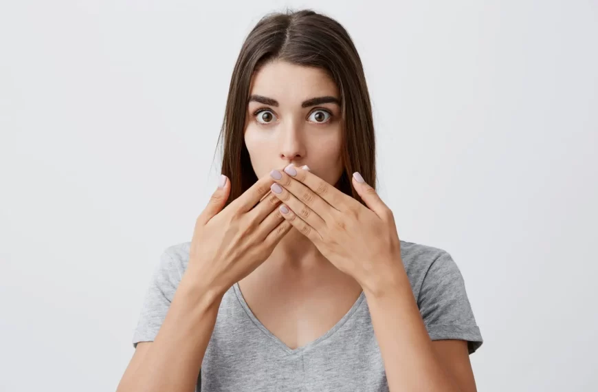 morena caucasiana-jovem com penteado-longo de roupas casual camiseta cinza com-as maos na boca e olhar-confuso e surpreso