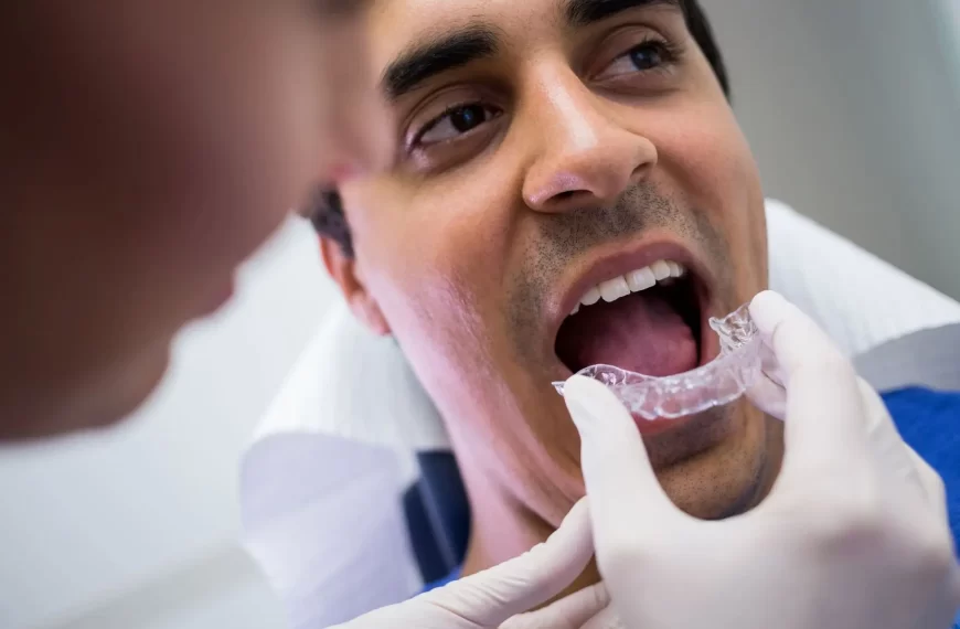 mostra um dentista com luvas, segurand um aparelho para dente trasnparente. O paciente está de boca aberta.